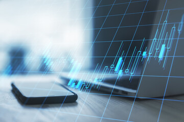 Investment concept with digital screen with candlestick at wooden table with smartphone and laptop background