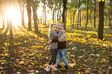 Cute children, a boy and a girl are walking and playing in the autumn forest.