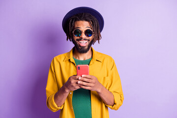 Photo of positive dark skin blogger typing post comment beaming smile isolated on violet color...