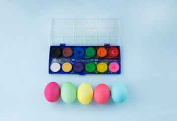 easter eggs dyed in pastel colors against light blue background and water color palette. Image with copy space. Easter decoration with kids concept