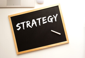 Text STRATEGY written in chalk on a slate board. Office desk.