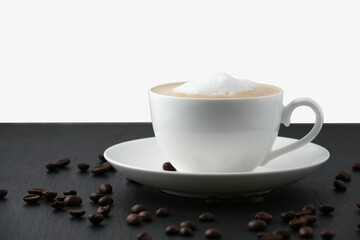 White cup with cappuccino on a black table, white background. Coffee beans on the table.