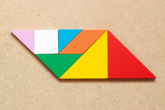 Color tangram puzzle in parallelogram shape on wood background