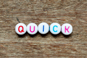 White bead with color letter in word quick on wood background
