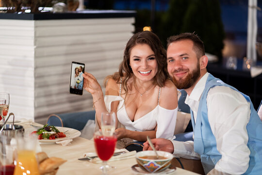 bride and groom look at photo on phone sitting at table at banquet.