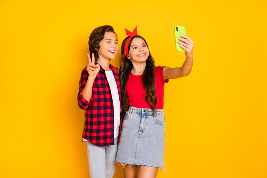 Photo of two children make selfie girl hold phone boy show v-up wear casual clothes isolated yellow color background