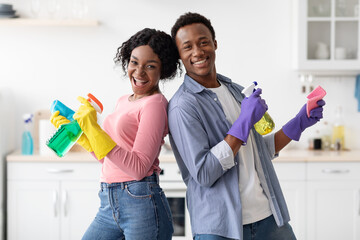 Joyful black couple with supplies for cleaning posing in kitchen