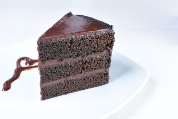 Decorated chocolate cake on white plate and light colored wooden background