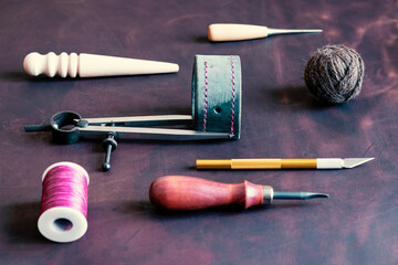 Tools for processing and creating leather products are laid out on the desktop in the leather workshop. In the center there is a blank of a leather product.