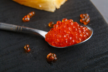 Spoon with red caviar on a black wooden background.