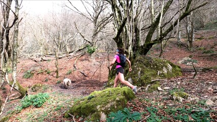 young woman trail running in the mountains with her dog