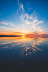 波の水たまりに反射した夕日と空と雲