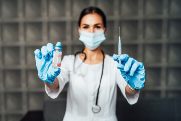 Naklejka premium The focus is on the nurse's hands in protective gloves holding the vaccine and the injection, in the background a nurse in a protective mask. Safe vaccination
