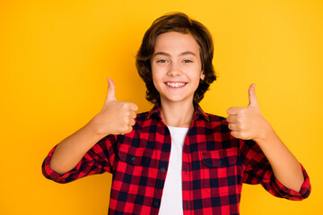 Photo of little cheerful boy raise two thumbs up wear checkered shirt isolated yellow color background © deagreez