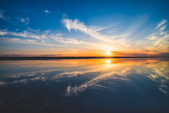 波の水たまりに反射した夕日と空と雲 © Kengo/ けんご