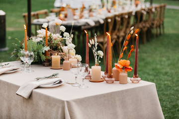 Candles, dried flowers and accessories, bouquets and glasses on table with linen tablecloth on newlywed table