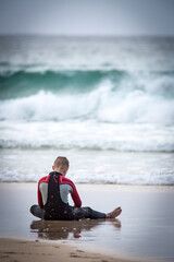Fototapeta premium person sitting on the beach in a wetsuit