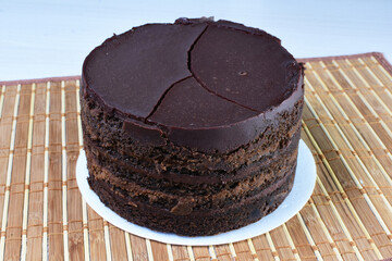 Decorated chocolate cake on white plate and light colored wooden background