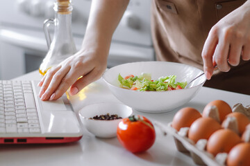 Obraz na płótnie Canvas Woman preparing a diet salad using digital cookbook. Fresh vegetables and laptop. Online cooking.