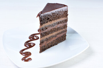 Decorated chocolate cake on white plate and light colored wooden background