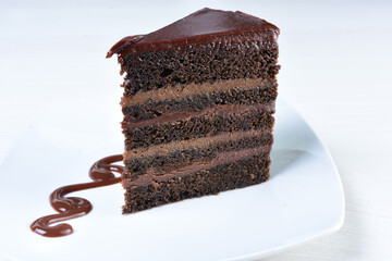 Decorated chocolate cake on white plate and light colored wooden background