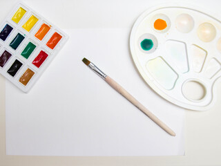 watercolor paints with a palette on a white sheet of paper a blank sheet of paper