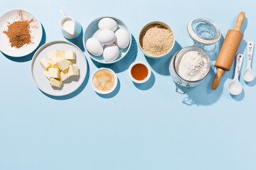Cooking baking background with ingredients, butter, flour, eggs, spices and utensils on blue table.