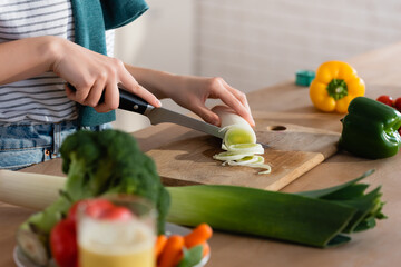 cropped view of woman cutting leek while preparing vegetable breakfast on blurred foreground