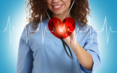 African-American cardiologist with stethoscope using virtual screen on color background