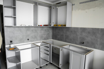 Custom kitchen cabinets installation without a furniture facades mdf. Gray modular kitchen from chipboard material on a various stages of installation in kitchen with a grey tile on floor and walls.