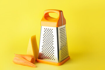 Metal grater, carrots and cheese on color background