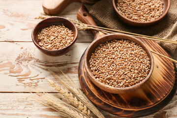 Bowls with wheat grains on light wooden background
