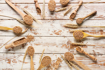 Frame made of scoops and spoons with wheat grains on light wooden background