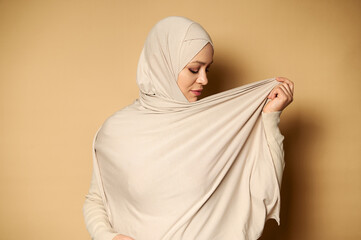 Side portrait of an elegant muslim woman wearing hijab. Strict formal outfit and elegant appearance. Islamic fashion. Beige background with copy space.