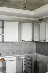 Custom kitchen cabinets installation without a furniture facades mdf. Gray modular kitchen from chipboard material on a various stages of installation in kitchen with a grey tile on floor and walls.