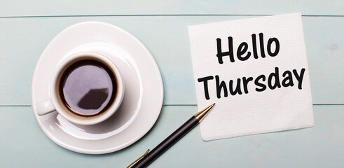 On a light blue wooden tray, there is a white cup of coffee, a handle and a napkin that says HELLO THURSDAY