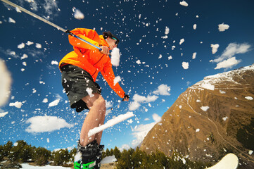 man skier in flight after jumping from a kicker in the spring against the backdrop of mountains and blue sky. Close-up wide angle. The concept of closing the ski season and skiing in spring - obrazy, fototapety, plakaty