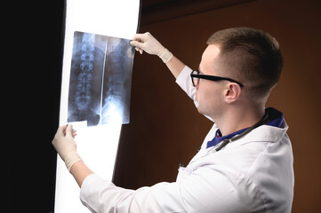 Portrait of a young doctor with glasses and a stethoscope around his neck against a wrinkled background. Holds an X-ray picture in his hands and looks at the camera with a slight smile