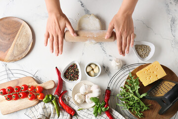 Woman making dough for pizza on light background