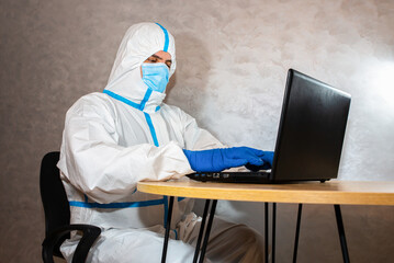 Doctor wearing medical protective suit, medical mask and gloves working on laptop. Protection mers by virus epidemic. Coronavirus (COVID-19). Healthcare concept. Remote work in a pandemic covid.