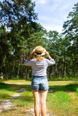Fototapeta premium Hipster girl in straw hat standing in the forest. Wanderlust concept. Travelling ideas. Beautiful woman in the nature. Summer vibes.