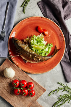 Grilled Fish With Lettuce And Tomatoes On A Round Orange Plate Top View