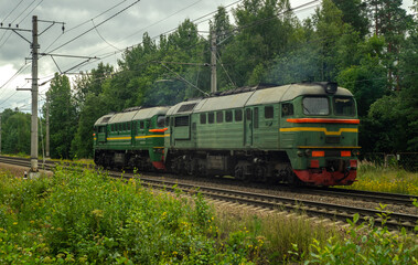 Naklejka premium An old green locomotive rides on the railway near the forest