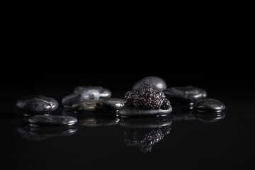 Caviar de esturión sobre piedra negra con reflejo en un fondo negro