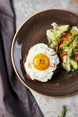 scrambled eggs and salad on a brown plate next to a wooden board with tomatoes and mushroom on a gray concrete background top view