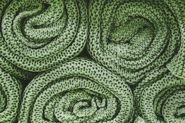 Green knitted blankets rolled into rolls. Knitted texture, factory textiles. Neat pile of rolled knitted warm clothing.