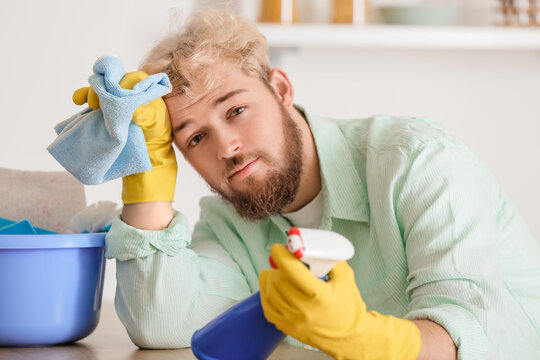 Tired young man with cleaning supplies in kitchen