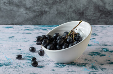 Bowl of black fresh grapes on colorful background