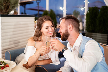newlyweds sit at table in restaurant and listen to congratulations from guests.