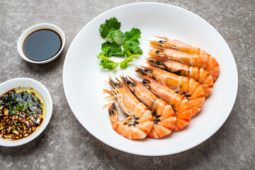 A plate of boiled black tiger prawns and seasoning sauce on cement shading